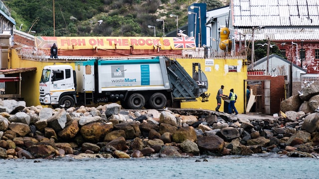 garbage truck picking up rubbish next to a sea