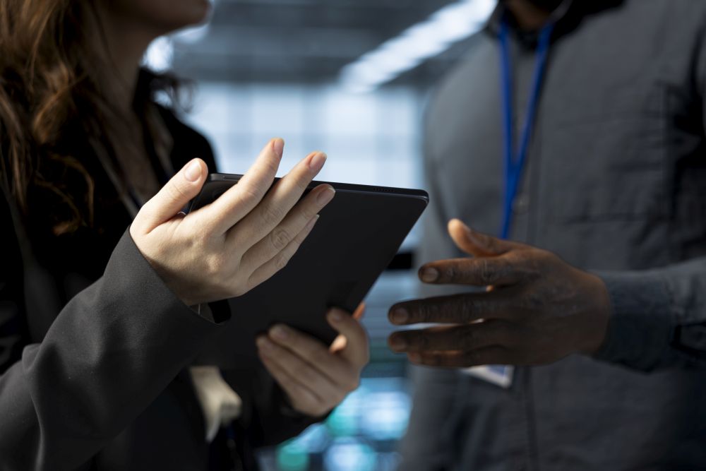 Two people are standing and discussing something related to tech recruitment Singapore while holding a tablet device in a professional setting.